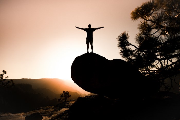 Silhouette of a person with arms outstretched on a rock at sunrise