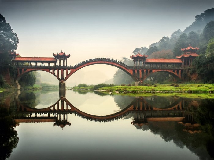 Covered bridge with pavilions reflected in water, China