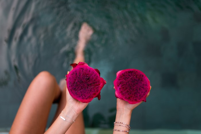 Woman holding dragon fruit halves in a pool