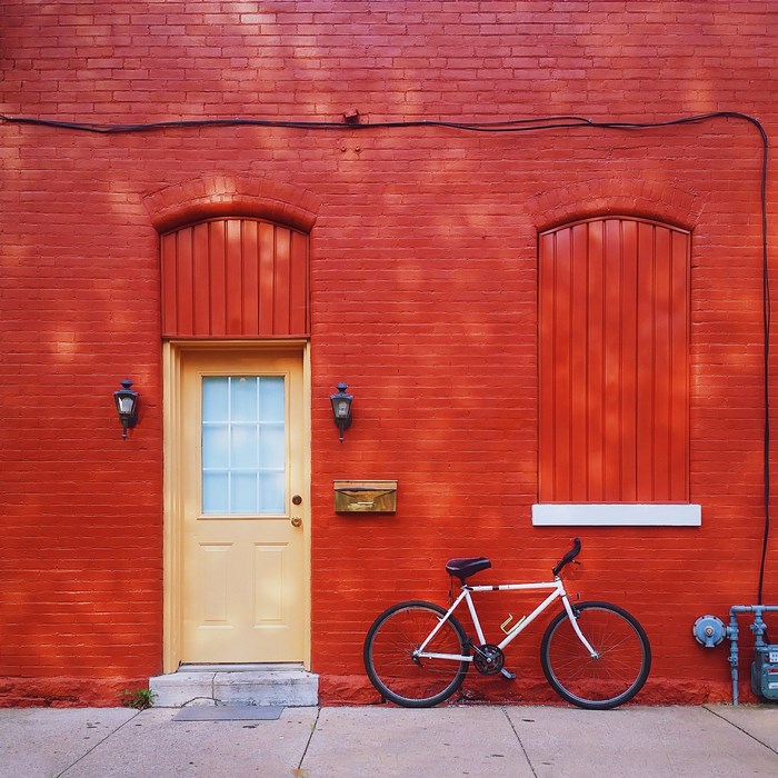 White bicycle parked by a red brick wall with a yellow door