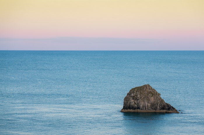 Rock in the ocean at sunset with pastel sky
