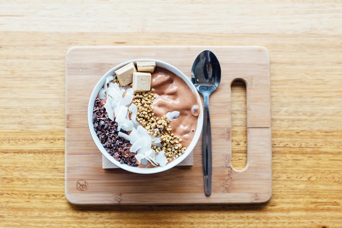 Smoothie bowl with coconut, cacao nibs, and granola on a cutting board