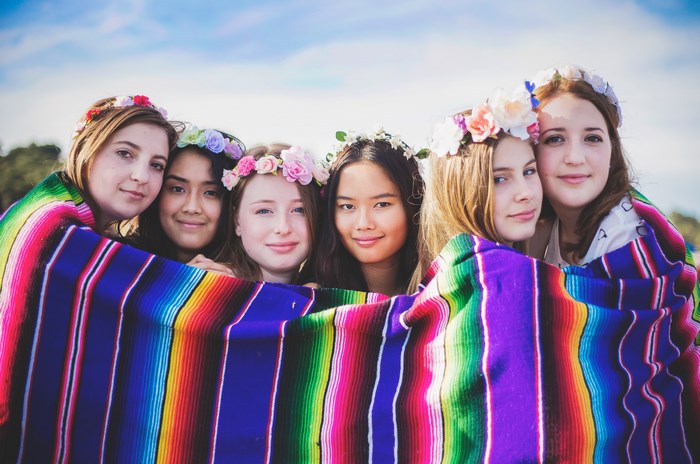 Six young women wearing flower crowns wrapped in a colorful blanket
