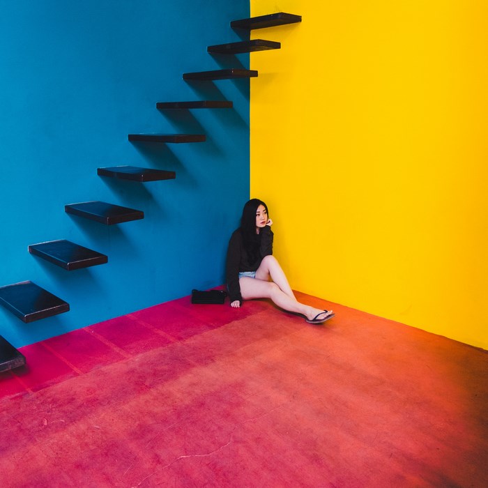 Young Asian woman sitting by a colorful wall with stairs