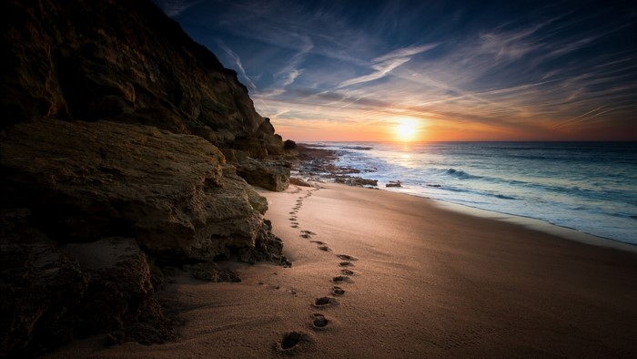 Footprints on a beach at sunset with a cliff