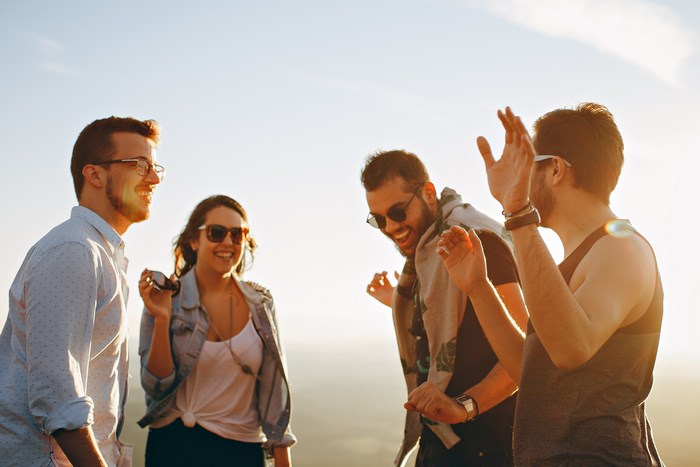Four friends laughing and dancing outdoors at sunset