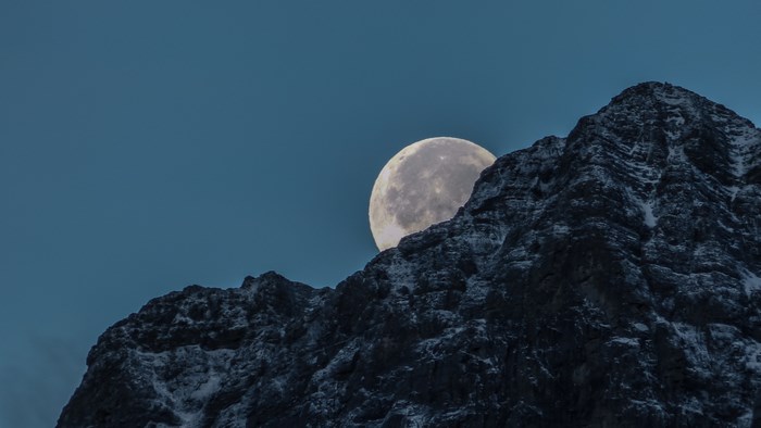 Full moon rising behind a snow-capped mountain