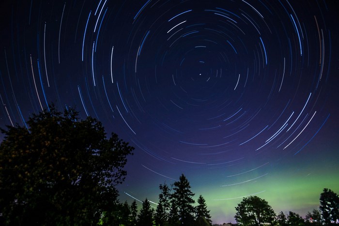 Star trails over trees with aurora borealis