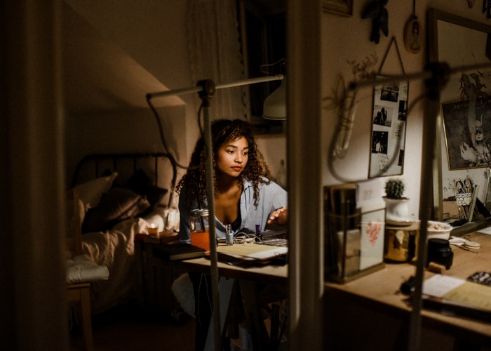 Woman working at a desk in a dimly lit bedroom