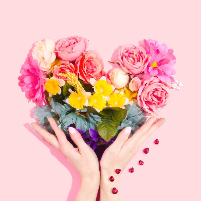 Hands holding a heart-shaped floral bouquet with ladybugs