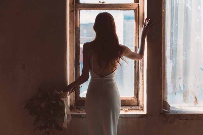 Woman in a wedding dress holding flowers by a window