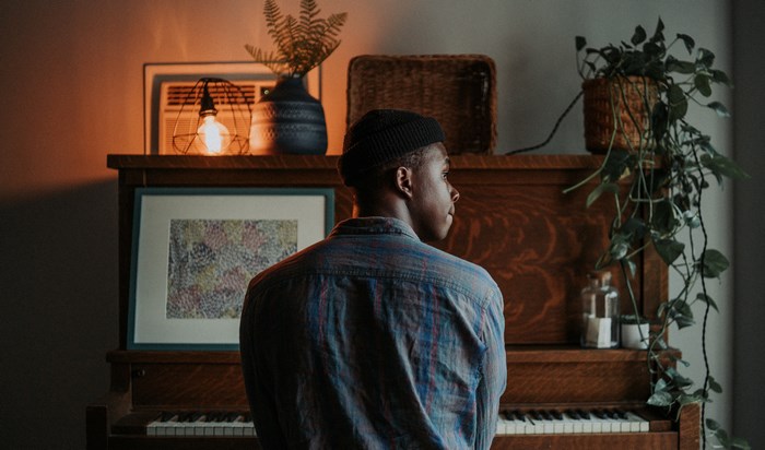 Man in beanie and plaid shirt sits at a piano
