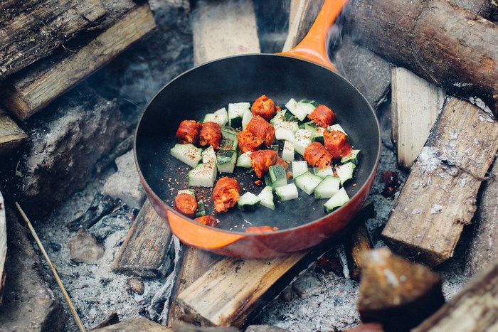 Chorizo and zucchini cooking in a skillet over a campfire
