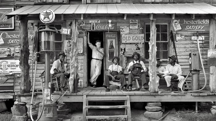 Men on the porch of a general store with gas pumps