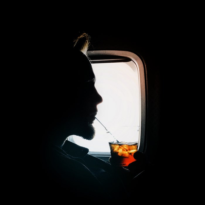 Silhouette of a man drinking from a glass on an airplane