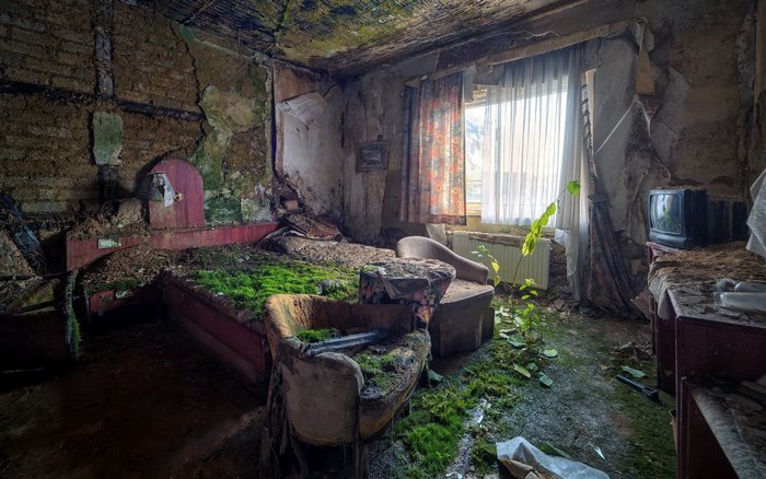 Overgrown abandoned hotel room with bed and TV