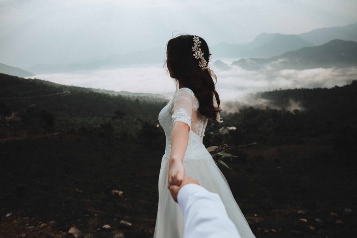 Bride in wedding dress holding hands in misty mountains