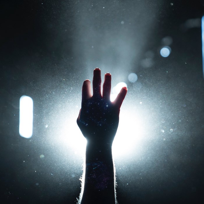 Silhouette of a hand raised against bright lights