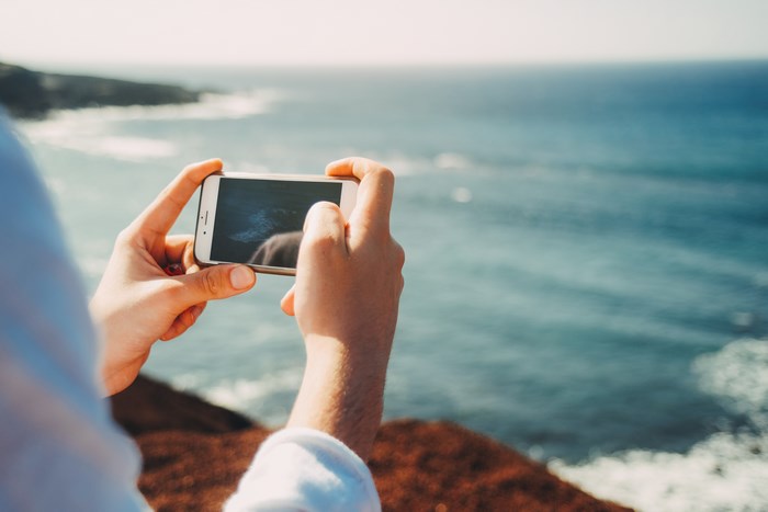 Person holding iPhone to capture ocean view