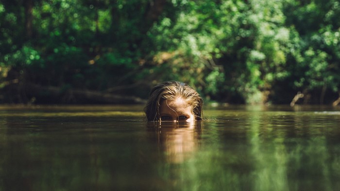 Woman peeking out of water in a forest