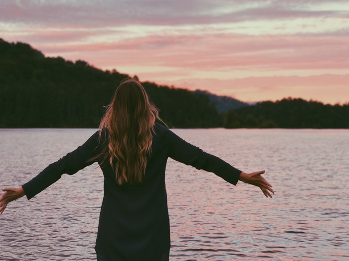 Woman with arms outstretched by a lake at sunset