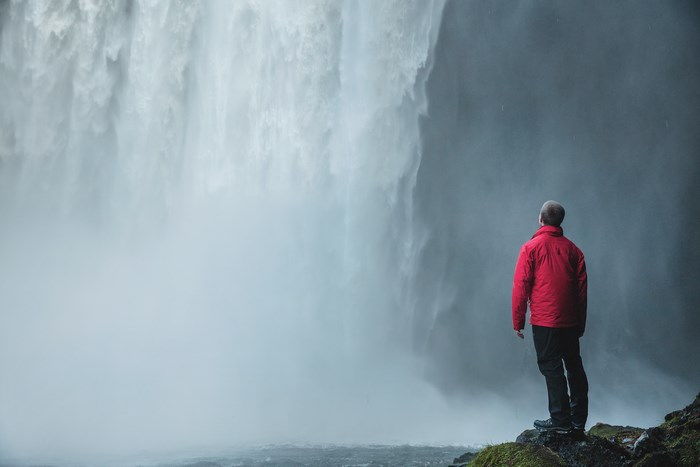 Man in red jacket standing by a waterfall