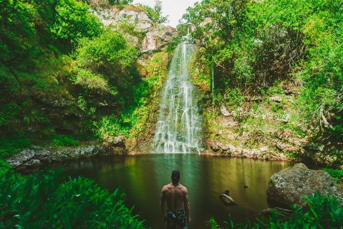 Man standing shirtless in front of a waterfall