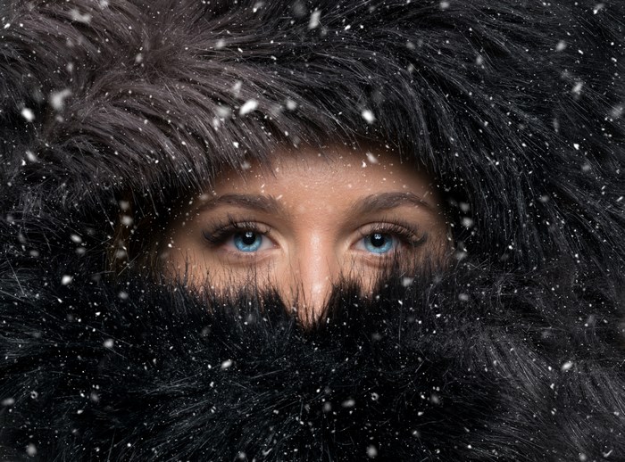 Close-up portrait of a woman in a fur coat during snowfall