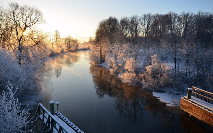 Winter sunrise over a frozen river with frosted trees