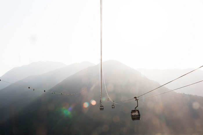 Cable cars ascend misty mountains under bright sunlight