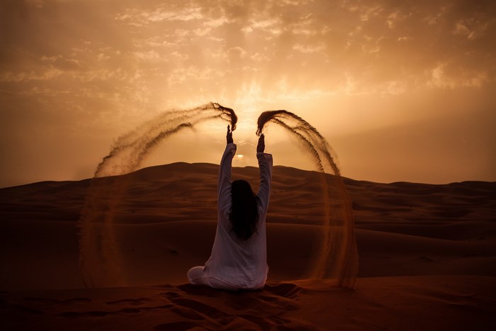 Woman throwing sand in the desert at sunset