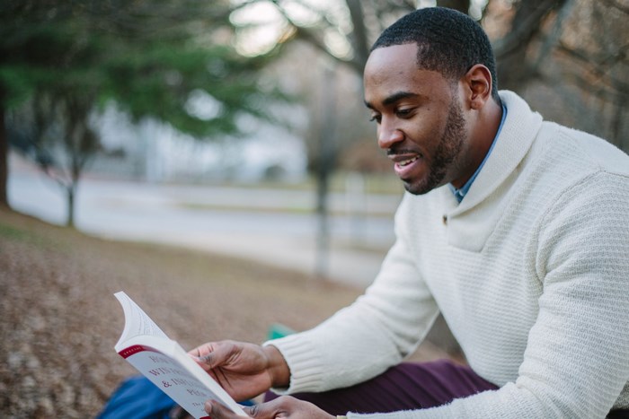 Man in sweater reading a book outdoors