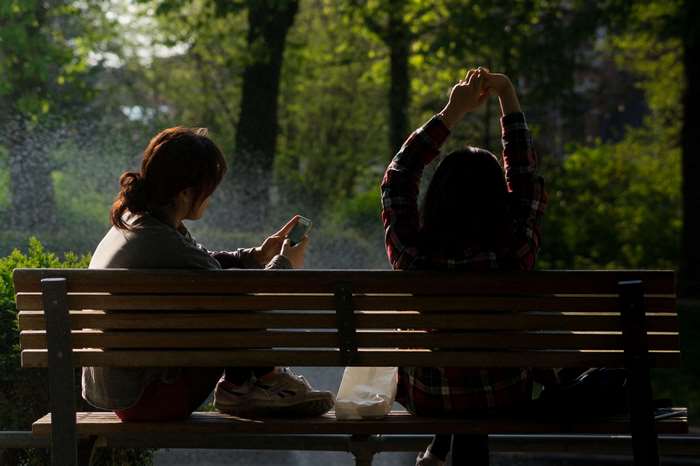 Two people sitting on a park bench with a smartphone