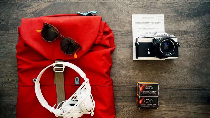 Travel essentials: backpack, sunglasses, headphones, camera, and permit
