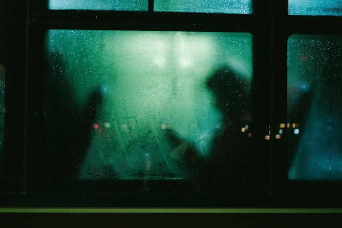 Silhouettes through a rainy bus window at night