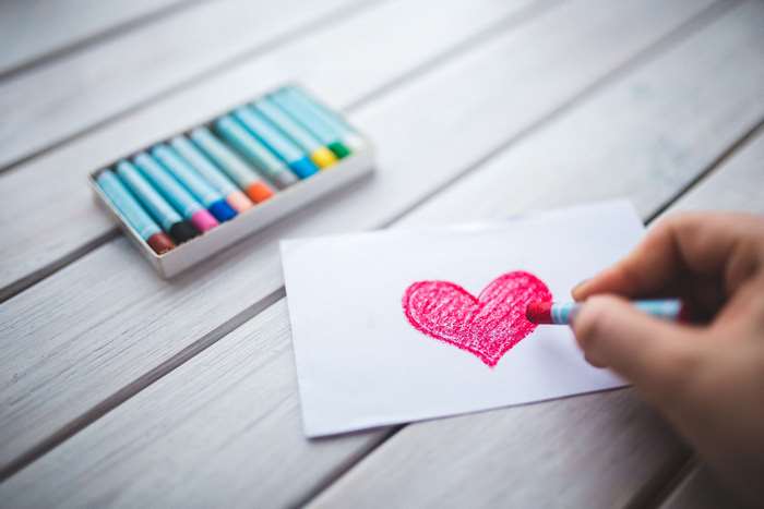 Hand drawing a red heart with crayons