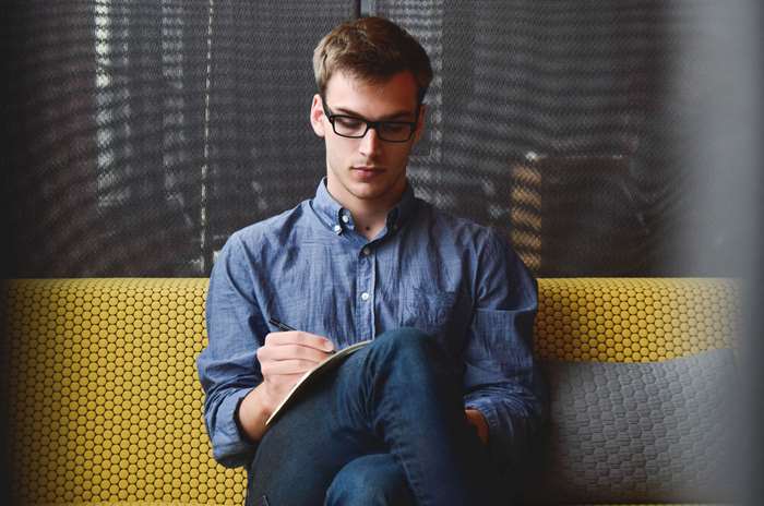 Man in blue shirt writing notes on couch