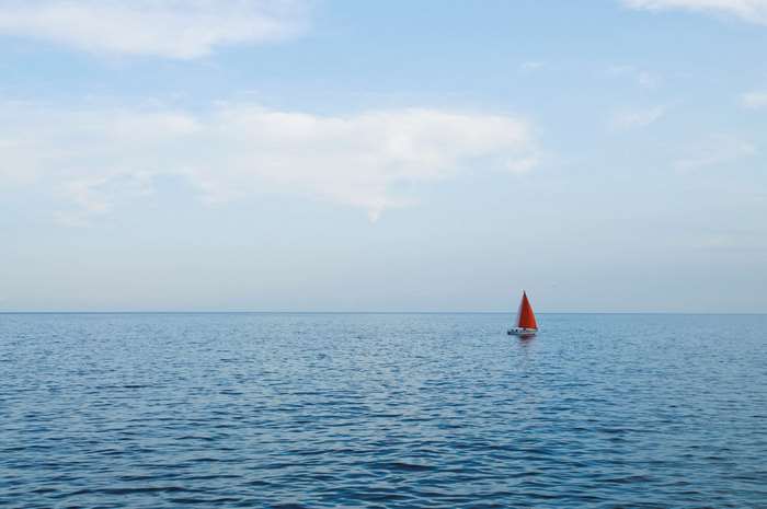 Sailboat with orange sail on the ocean horizon 4K