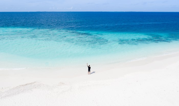 Man waving on a white sand beach in the Maldives