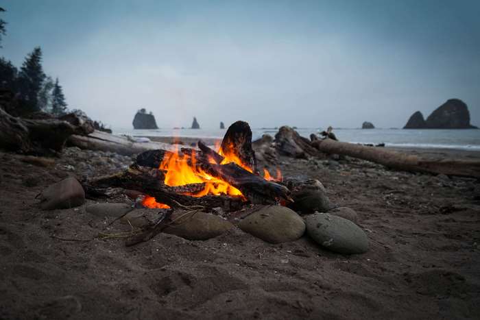 Campfire on a beach with ocean and rock formations