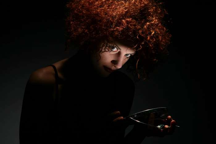 Woman with curly reddish hair holding glasses