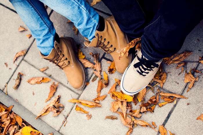 Two people wearing boots and sneakers among autumn leaves