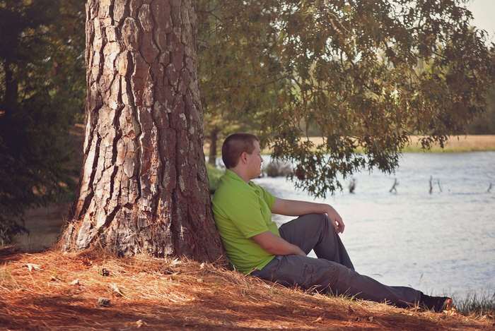 Man sitting by a tree near a lake