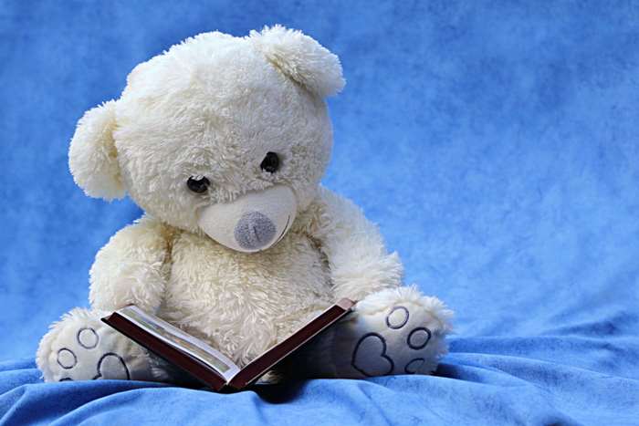 White teddy bear reading a book on a blue cloth