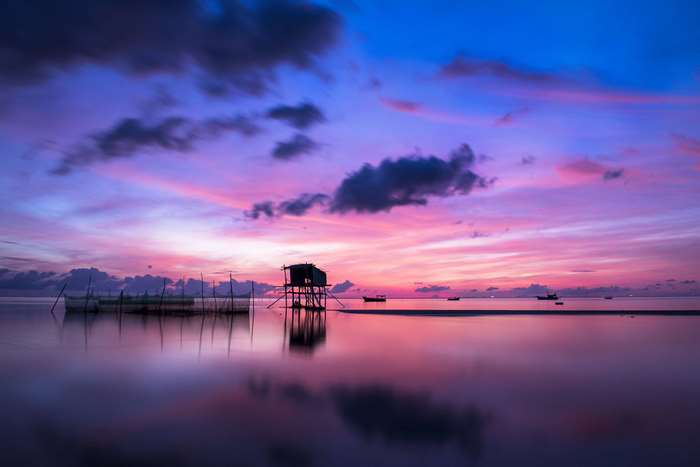 Tropical beach at sunrise with fishing hut and boats