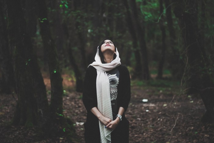 Woman in scarf looking up in a dark forest
