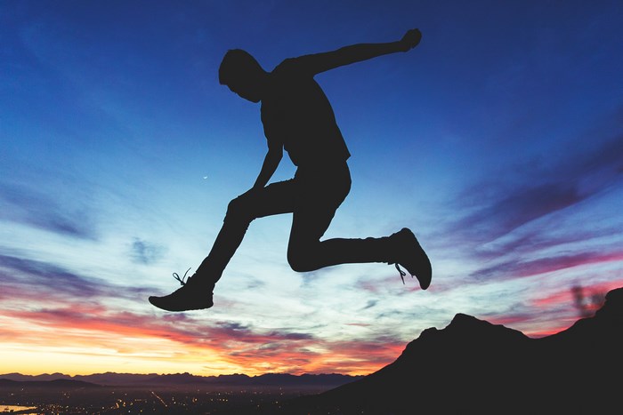 Silhouette of a man jumping over a mountain at sunset
