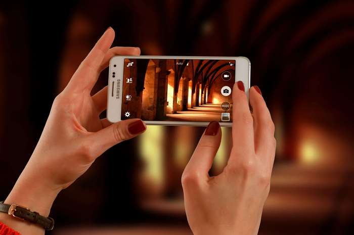 Hands holding Samsung smartphone taking photo of arched hallway
