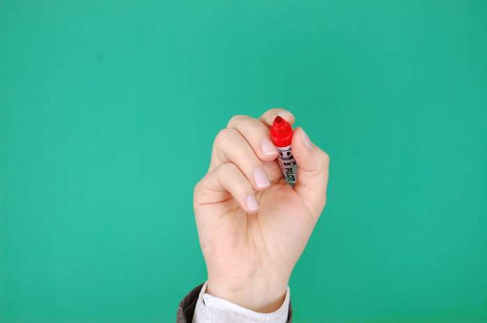 Hand holding a red Pilot marker on a green background