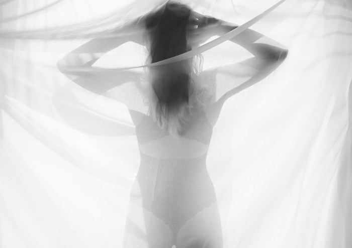 Silhouette of a woman in lingerie behind a sheer curtain